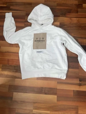 ÄKTA Vit hoodie från Burberry - Snygg vit hoodie från Burberry med klassisk huva och ribbade muddar. Märket syns tydligt framtill och på etiketten i nacken. Perfekt för dig som gillar stilrena och exklusiva plagg. Materialet är mjukt och bekvämt, troligen bomull. (Passar upp till M men är S)
