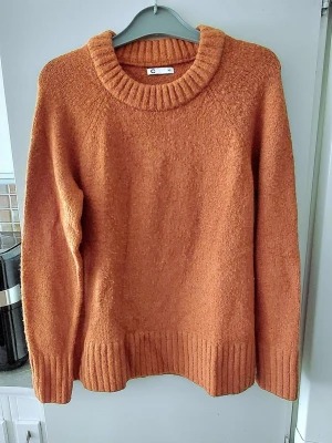 Senapsgul stickad tröja från Xs/s - Mysig rostbrun stickad tröja från Cubus med grov ribbad rund halsringning, muddar vid ärmslut och nederkant. Tröjan har en avslappnad passform och är perfekt för kyliga dagar. Materialet känns mjukt och värmande. Storlek XS/S. Lös passform. Den sista bilden visar tröjans rätta färg bäst.