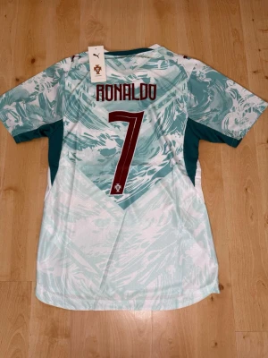Ronaldo #7 – Player Edition Portugal (storlek M) - Ronaldo #7-tryck. Player Edition Portugal. Storlek M. Helt ny och aldrig använd. Säljs i befintligt skick. Skickas snabbt! 🚚💨  Mått för denna tröja (storlek M): (Uppmätta av leverantör – viss variation kan förekomma) • Halva bröstmåttet: 51 cm • Tröjans längd: 72,5 cm • Ärmbredd: 22,5 cm • Axelbredd: 43 cm • Ärmlängd: 39 cm • Manschettbredd: 18 cm  🔥 Player Edition-modell – tajtare passform än vanliga supportertröjor. 🇵🇹 Portugal landslag.