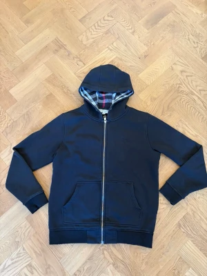 Burberry Hoodie  - Svart Burberry zip hoodie med klassisk rutig detalj i huvan och stilren design. Väldigt skön och lätt att matcha till olika outfits. Märkt M men sitter mer som en S. Fint skick.