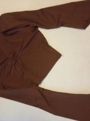 Brun långärmad topp med v-ringning - Snygg brun långärmad topp med v-ringning och rynkdetalj framtill. Toppen har en spetsig nederkant som ger en cool och trendig look. Perfekt att styla med jeans eller kjol för en modern outfit.
