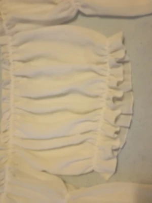 Vit offshoulder blus med volanger - Supersöt vit offshoulder blus med volangdetaljer och smockad resår både upptill och nertill. Långa puffiga ärmar med resår vid handlederna ger en romantisk vibe. Perfekt att styla med jeans eller kjol för en trendig look.