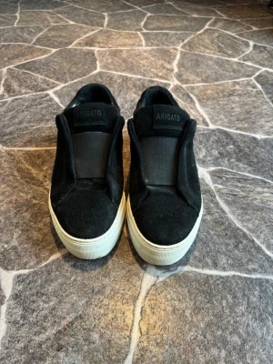 Svarta clean 360 Axel Arigato skor - Svarta slip-on sneakers från Axel Arigato med ovandel i mocka och bred resår över vristen. Tjock vit sula och diskret logga på sidan. Sköna och stilrena skor som passar till det mesta. Storlek 38 och knappt använda.