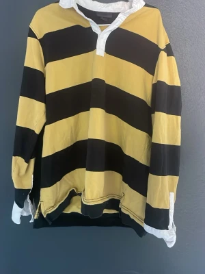 H&M Skjorta - Cool långärmad rugbytröja med breda gula och svarta ränder samt vit krage och manschetter. Oversized passform och klassisk look, perfekt för en avslappnad stil.