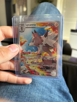 Pokémonkort Lycanroc holografisk - Säljer ett holografiskt Pokémonkort med Lycanroc från Scarlet & Violet-serien. Kortet har färger i rött, vitt och blått med glittrande effekt och är på engelska. Det är nummer 166/193 och har coolt motiv med Lycanroc i fokus. Perfekt för samlare eller Pokémonfans!