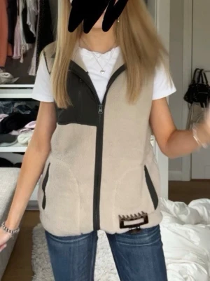 Beige fleeceväst med svarta detaljer - Säljer en beige fleeceväst med svarta detaljer och dragkedja framtill. Aldrig använt den❤️