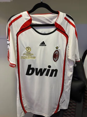 AC Milan Kaka' Champions League tröja - Vit AC Milan matchtröja från Adidas med röda och svarta detaljer, Champions League-final 2007-tryck, Bwin sponsorlogga och Kaka' 22 på ryggen. Tröjan har klubbmärke och Adidas-logga på bröstet. Perfekt för fotbollsfans!