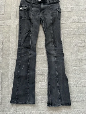 Svarta lågmidjade bootcut jeans med fickdetaljer - Snygga svarta bootcut jeans med vita sömmar och coola fickdetaljer på sidorna. Jeansen har en lätt utsvängd passform och diskreta ränder i tyget som ger en unik look. Perfekta för dig som vill ha en trendig och avslappnad stil.