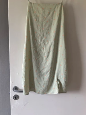 Ljusgrön blommig mini klänning  - Söt miniklänning i ljusgrönt med små  blommor och smala axelband. Klänningen har en slits framtill och ett flowigt fall, perfekt för varma dagar. Materialet känns lätt och luftigt. satin