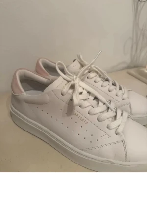 Axel Arigato skor - Vita sneakers från Axel Arigato i modellen The clean 90 med ljusrosa mockadetalj på hälen och guldfärgad logga på sidan. Nypris 2650kr!💕 Använda ca. 4-5 gånger. Storlek 41 men små i storleken så passar 40 perfekt! Pris kan diskuteras!