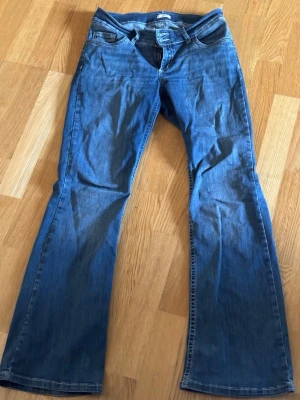 Blå bootcut jeans från Nelly - Snygga blå bootcut jeans från Nelly med klassisk femficksdesign och dubbla knappar i midjan. Jeansen har utsvängda ben och är tillverkade i denim med lätt tvättad look. 