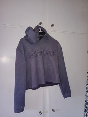 Lila hoodie med texten WHATEVER - Säljer en lila hoodie med huva och broderad texten 'WHATEVER' på bröstet. Hoodien har en avslappnad passform och långa ärmar. Perfekt för dig som gillar en chill och trendig stil.