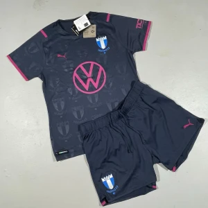 MFF officiellt match-set - Puma / Malmö FF officiellt kit i mörkblått med rosa detaljer för dam. Kortärmad matchtröja och shorts, båda med klubbmärke och tryckta loggor. Materialet är lätt och andas med Pumas DRYCELL funktion, perfekt för fotbollsträning eller match.