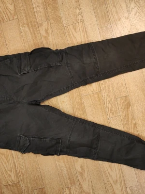 Svarta cargobyxor från H&M stl herr S - Svarta cargobyxor från H&M med relaxed fit. Byxorna har flera stora fickor på benen och är tillverkade i ett mjukt bomullsmaterial. Perfekta för en avslappnad och trendig streetstil. Herr stl S