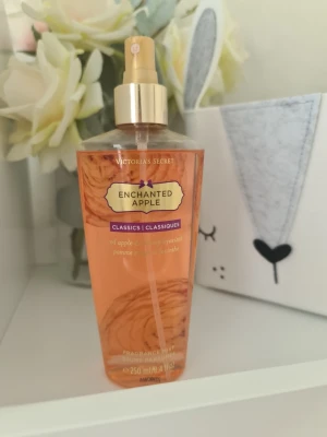 Victoria's Secret Enchanted Apple mist - En fräsch doftmist från Victoria's Secret i doften Enchanted Apple. Flaskan är genomskinlig med röd-orange vätska och har en guldfärgad spraypump. Innehåller 250 ml och har inslag av röd äpple och saftig hyacint.Säljer nu av min vintage kollektion. Perfekt för samlare. Eftersom dofterna är vintage kan lukten skilja sig markant från nya, och köps därmed på eget bevåg.