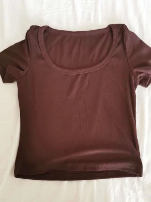 Brun ribbad topp med kort ärm - En basic brun ribbad topp med korta ärmar och rund halsringning. Perfekt att styla med jeans eller kjol för en enkel och snygg look. Materialet är stretchigt och sitter tajt mot kroppen.