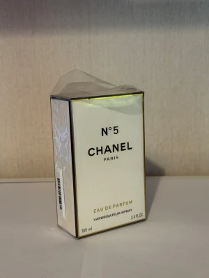 Chanel No 5 Eau de Parfum 100ml - Chanel No 5 Eau de Parfum i klassisk vit och guldig kartong med svart text. Parfymen är en ikonisk doft från Chanel Paris och kommer i en 100 ml förpackning. Lyxig och tidlös design som passar perfekt för dig som gillar exklusiva parfymer.
