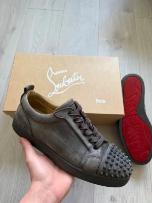 Louis Junior Spikes - Grå sneakers med nitar från Christian Louboutin. Generellt väldigt fint skick, nån enstaka fläck i mockan kan synas vid nära inspektion. Kommer med Box, extra snören, dustbags, kvitto och orderbekräftelse från Mytheresa. 