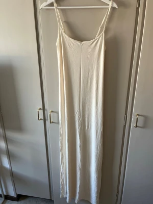 Krämvit långklänning med smala axelband - En stilren krämvit långklänning i soft touch serien från Gina Tricot som formar sig efter kroppen. Aldrig använd bara testat. 