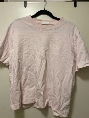 Ljusrosa basic t-shirt från Gina Tricot - En enkel och stilren ljusrosa t-shirt i mjuk bomull. T-shirten har rund halsringning och korta ärmar, perfekt för en avslappnad look. Passformen är normal och tyget känns skönt mot huden.