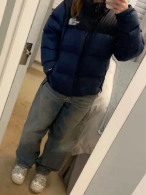 Blå pufferjacka från The North Face - Säljer en blå och svart pufferjacka från The North Face med hög krage och dragkedja framtill. Jackan har två sidofickor med dragkedja och logga på bröstet. Perfekt för kalla vinterdagar och riktigt skön att bära. Klassisk puffig passform och dunfylld för extra värme.  Nypris 3899kr💗