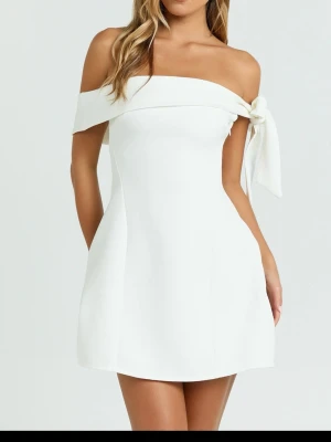 Vit klänning - Superfin vit kort klänning med offshoulder-design och en snygg rosettdetalj på ena axeln. Klänningen har en enkel, stilren form och är perfekt för sommarens alla tillfällen. Materialet känns mjukt och följsamt mot kroppen. Perfekt till sommaren elelr studenten. 