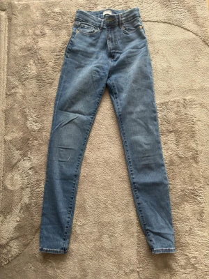 Grå high waist skinny jeans - Snygga grå high waist skinny jeans med klassisk femficksdesign och smal passform. Jeansen har dragkedjegylf och knapp framtill samt bälteshällor. Perfekta för en trendig och avslappnad look.