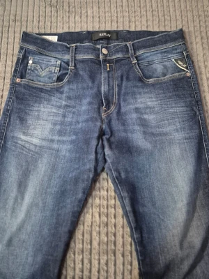 Replay jeans  - Snygga blå jeans från Replay med klassisk femficksdesign och slitna detaljer framtill. Jeansen har en medelhög midja och raka ben. Tydliga kontrastsömmar och Replay-logga på myntfickan ger en cool touch. Perfekta för en avslappnad streetstil.