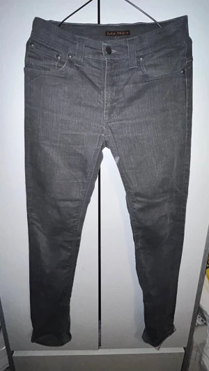 Gråa jeans från Nudie Jeans - Snygga gråa slim-fit  jeans från Nudie Jeans med klassisk femficksdesign och dragkedja. Jeansen har en smal passform och är tillverkade i ett mjukt denimtyg som sitter skönt. Perfekta för en stilren och modern look. 98% bomull och 2% EA, Thin Finn. Dry grey. W30 L32