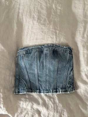 Denim tubtopp i ljusblå jeans - Trendig tubtopp i ljusblå denim med markerade sömmar och klassisk jeanslook. Perfekt för att skapa en cool och avslappnad stil. Axelbandslös modell som sitter snyggt och ger en edgy vibe.