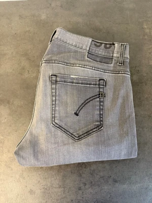 Grå slim fit jeans från Dondup W36 - Snygga grå jeans i slim fit-modell med klassiska fem fickor och råa, avklippta benslut. Jeansen har en diskret tvättad look och svarta detaljer på bakfickan. Perfekta för en trendig och avslappnad stil. Hör av dig om du vill ha alla mått!
