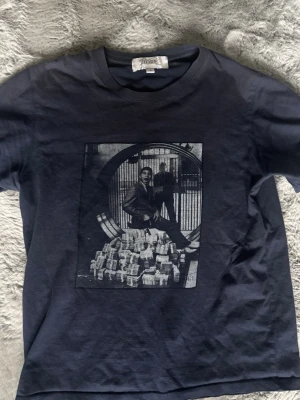 Marinblå t shirt med tryck - Cool svart t-shirt från Fiore studios med ett stort grafiskt tryck på bröstet som föreställer en man framför ett kassavalv och högar av pengar. Klassisk rund hals och korta ärmar. .