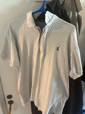 Vit pikétröja Polo Ralph Lauren special edition  - Vit pikétröja från Polo Ralph Lauren med små färgade kungarkronor och klassisk krage. Perfekt för sommaren med storlek XL men sitter som L. Priset kan diskuteras. Levereras inom 24 tim.