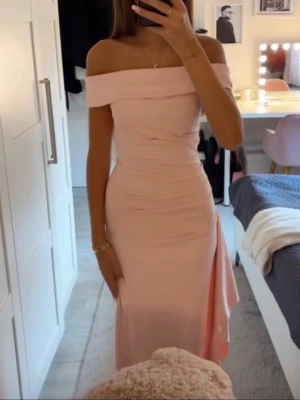 Ljusrosa offshoulder balklänning  - Säljer en elegant ljusrosa balklänning med offshoulder-design och slits på sidan. Klänningen har en figurnära passform och är perfekt för speciella tillfällen. Materialet känns mjukt och följsamt mot kroppen.