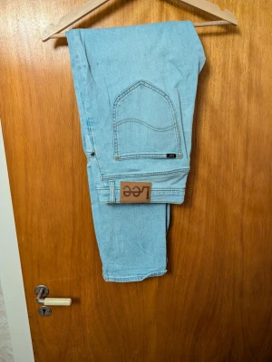 Ljusblå Lee jeans med rak passform - Säljer ett par klassiska ljusblå jeans från Lee med rak passform. Jeansen har fem fickor, Lee-lapp i läder baktill och är tillverkade i bomullsdenim. Perfekta för en avslappnad och trendig look.