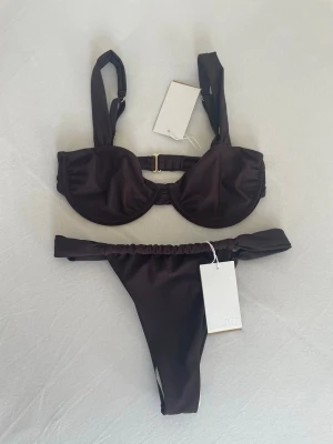 Ny bikini  - Säljer en helt ny oanvänd bikini från NAKD. Den är ju en jättefin brun färg med guldiga detaljer. Överdelen är i strl 70C och underdelen är i strl S.