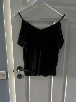 Svart offshoulder topp med smala band - Snygg svart offshoulder topp med smala axelband och v-ringning både fram och bak. Tunn och mjuk, perfekt till sommaren. Enkel att matcha med jeans eller kjol för en trendig look.