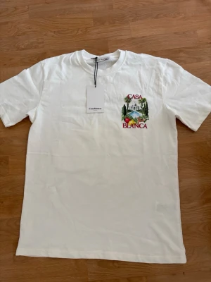Vit Casa Blanca t-shirt med tryck - Vit t-shirt från Casablanca med färgglatt tryck av palmer, frukter och byggnad samt texten 'Casa Blanca' på både bröstet och ryggen. Klassisk passform och rund halsringning. Perfekt för en trendig och avslappnad stil. Oversize