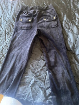 Svarta mjukisbyxor med fickor - Svarta mjukisbyxor i skön velour med bred resår och dragsko i midjan. Byxorna har två stora fickor fram och två bakfickor med knappar. Perfekta för chill och avslappnade dagar.