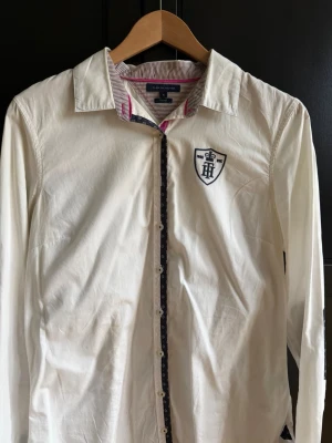 ,Vit skjorta Tommy Hilfiger, Fitted - Vit skjorta från Tommy Hilfiger med fitted passform. Skjortan har rosa detaljer och mönstrade armbågslappar. Tillverkad i bomull och har knappar framtill.