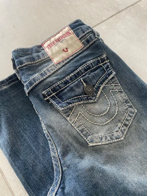 True Religion wide leg jeans blå baggy Bobbi  - Säljer ett par blå jeans från True Religion med breda ben och coola kontrastsömmar. Jeansen har klassisk femficksdesign, stor ficka bak med lock och logga på bakfickan. Materialet är slitstarkt denim i bomull. Perfekta för en avslappnad streetstil. Mått 📏 Totallängd: 100cm Midjelängd: 37cm Innersömmlängd: 76cm Lårviddlängd: 28cm Skador 🔧: Små skador vid benöppningarna, annars är de i perfekt skick   Storlek 🧍: 24   Passform: Bobbi (Super Baggy)  Jag kan förhandla mig till lägre pris.🙋💵 Om du har