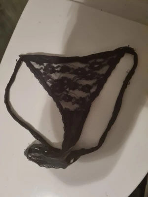 Svarta spetsstringtrosor - Säljer ett par svarta stringtrosor i transparent spetsmaterial med blommigt mönster. Trosorna har en smal passform och är tillverkade i mjuk och stretchig spets som ger en snygg och bekväm look.