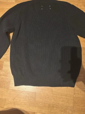 Svart ribbstickad tröja Maison Margiela - Säljer en svart ribbstickad tröja från Maison Margiela. Tröjan har rund halsringning, långa ärmar och de ikoniska vita sömmarna i nacken. Perfekt för dig som gillar minimalistisk och stilren design.