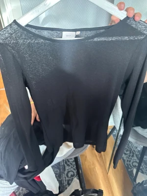 Svart långärmad topp från Nelly - Snygg svart långärmad topp från Nelly med rund halsringning. Tunn och lätt i materialet, perfekt för lager på lager eller som den är. Enkel och stilren design som passar till många olika outfits.