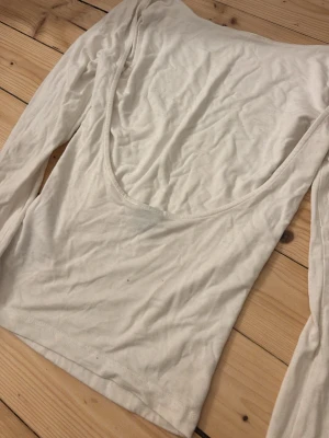 Vit långärmad topp med öppen rygg - Säljer en vit långärmad topp med djup, öppen rygg. Toppen är enkel och stilren, perfekt att matcha med olika outfits. Tillverkad i mjukt bomullsmaterial för en bekväm känsla.