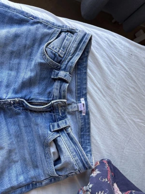 Blå bootcut jeans med dubbla bälteshällor - Säljer ett par ljusblå bootcut jeans med coola dubbla bälteshällor och klassiska femficksdetaljer. Jeansen har en snygg tvättad look och är tillverkade i denim. Perfekt för dig som gillar en avslappnad och trendig stil. Pga åter skick så kommer de tillbaka till mig i veckan. Innerbenet: 175 