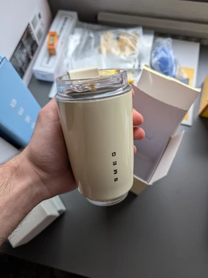 Beige termosmugg från Smeg - Snygg beige termosmugg från Smeg med lock i plast och stilren design. Muggen har Smeg-loggan tryckt vertikalt och kommer i originalförpackning. Perfekt för kaffe eller te på språng.