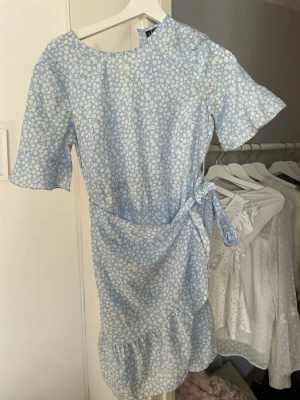 Klänning - En ljusblå klänning med volang och blommigt mönster i storlek XS från Vero Moda. Endast använd ett fåtal gånger.
