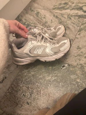 New Balance vita sneakers - Snygga vita sneakers från New Balance med grå detaljer och klassisk mesh-design. Skorna har en låg profil och den ikoniska N-loggan på sidan. Perfekta för dig som gillar sportig och clean stil.