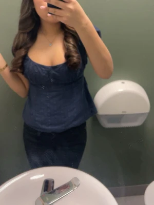 Mörkblå blus med knappar - Snygg mörkblå blus med korta puffärmar och knappar framtill. Toppen har en feminin v-ringning och lätt figursydd passform som framhäver midjan. Perfekt att styla med jeans eller kjol för en trendig look.